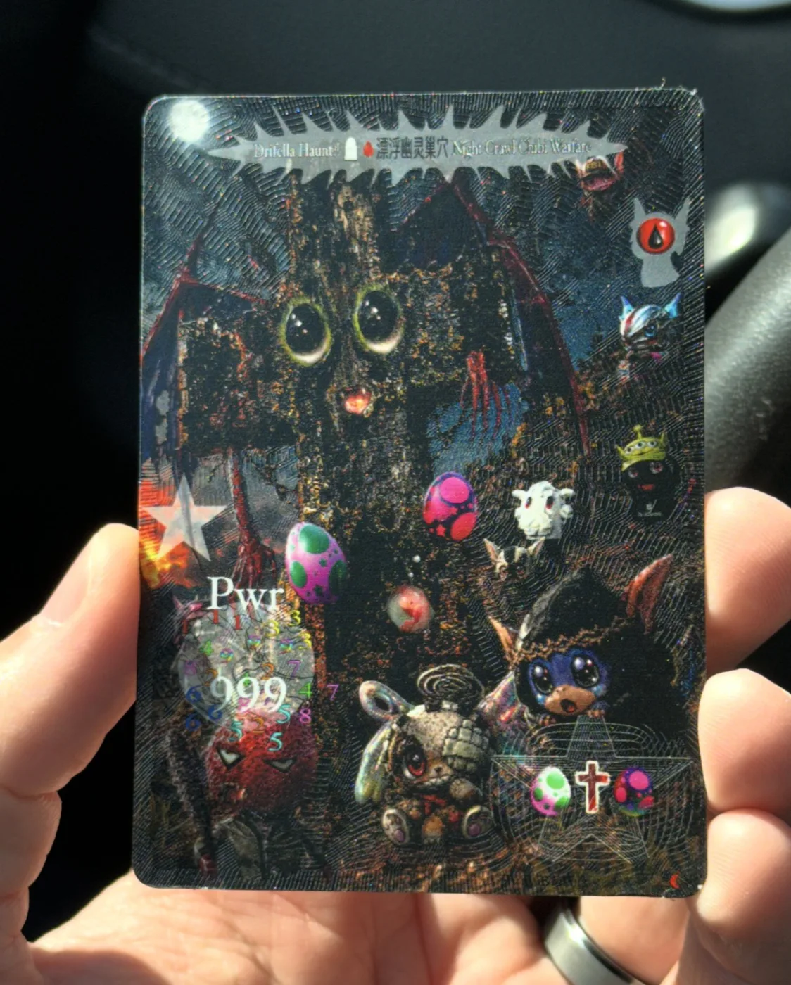 A clear acetate card held in hand, dense with chibi cats and charms, by Evil Biscuit. Edition of 100.
